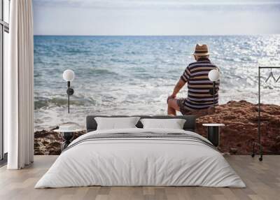 Italy, Sicily, Cava D'aliga, senior man sitting at the coast and looking to the sea Wall mural