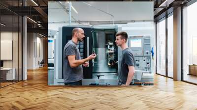 Maintenance engineer giving instruction to coworker while standing against machinery at industry Wall mural