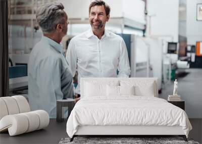 Mature businessman holding smart phone while discussing with colleague in industry Wall mural