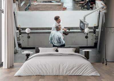 Mature male engineers discussing over manufacturing equipment in factory Wall mural