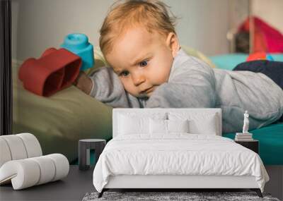 Portrait of baby girl lying on bed playing with plastic toy Wall mural