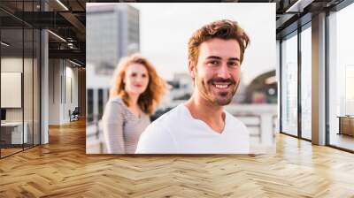 Portrait of happy young man with girlfriend in the background at sunset Wall mural