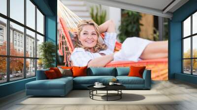 Portrait of smiling mature woman relaxing in hammock on terrace Wall mural