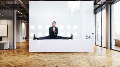 Smiling businessman doing the splits on reception desk in office Wall mural