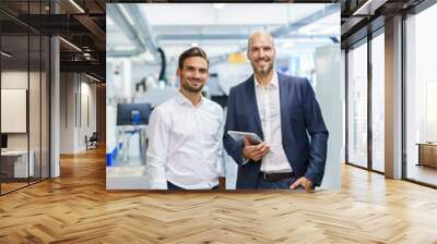 Smiling mature businessman holding digital tablet while standing by young male engineer at factory Wall mural