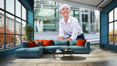 Smiling senior businesswoman sitting outside looking around Wall mural