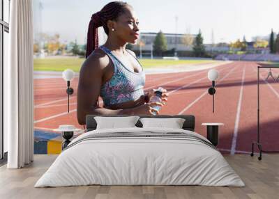 Thoughtful female sportsperson holding energy drink bottle on sports track during sunny day Wall mural