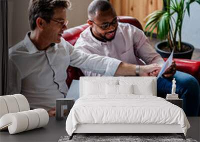 Two businessmen using laptop and discussing documents on sofa in loft office Wall mural