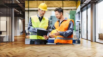 Two men wearing protective workwear holding clipboard and talking in factory Wall mural