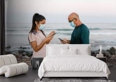 Woman and senior man with face mask using phone while standing against sea Wall mural