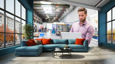 Young businessman using laptop in production hall Wall mural