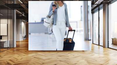 Young businesswoman texting with her mobile phone while walking with suitcase on the hall of the train station Wall mural