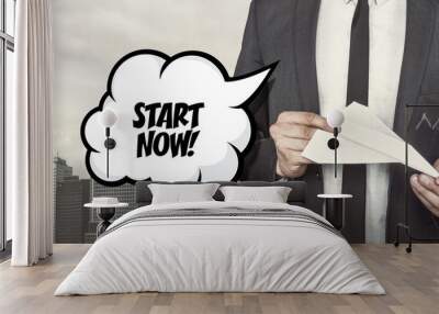 Start now text on speech bubble with businessman holding paper plane in hand Wall mural