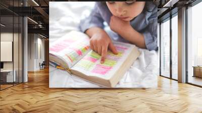 Little girl reading from Bible while lying in bed. Bible with marks on letters. Wall mural