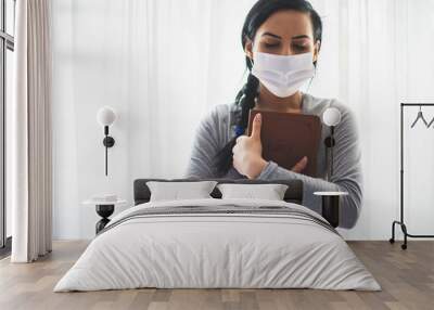 Portrait of a woman with a surgical mask on her face and a bible held tight to her chest Wall mural