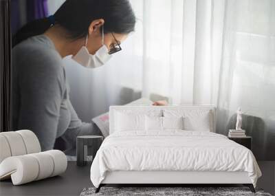 Quarantined woman with mask reading from bible and praying Wall mural