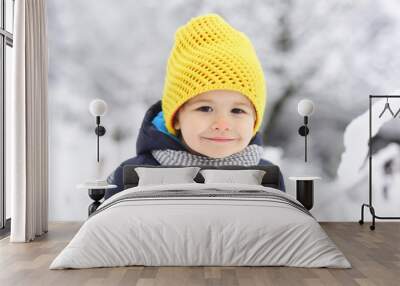 Cheerful kid smiling in winter snow park. Portrait of happy joyful beautiful little boy on white background of snowing trees. Happy childhood on walk, child smile to camera. Beautiful child portrait Wall mural