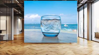 Cool drink on table with tropical beach setting behind. Wall mural