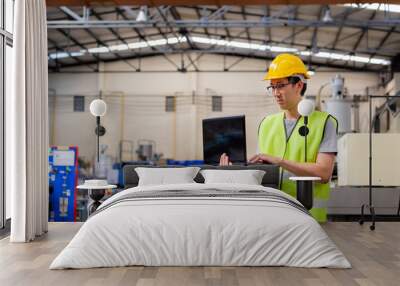 Asian male Industrial engineer in hard hat working with laptop in safety jacket at heavy industry manufacturing factory. Processing plastic injection molding industry Wall mural