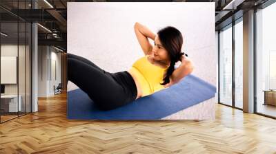 Close-up of young active and fitness Asian woman doing sit ups and crunches inside gym with exercise ball in background. Wall mural