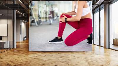 Close up of young fit and active woman in sportswear suffering knee pain accident during workout indoors gym . Wall mural