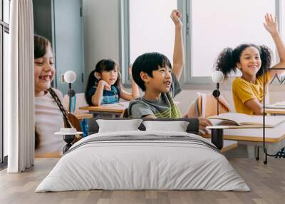 Elementary age Asian student boy raised hands up in class. Diverse group of pre-school pupils in elementary age in education building school. Volunteering and participating classroom concept. Wall mural