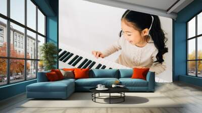 From above of happy smiling cute Asian girl playing piano enjoying time practicing music at home Wall mural