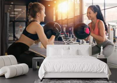 Happy young female athletic people performing squat exercises with friend and holding a medicine ball at fitness gym. Group of two confident women with healthy lifestyle working out together Wall mural