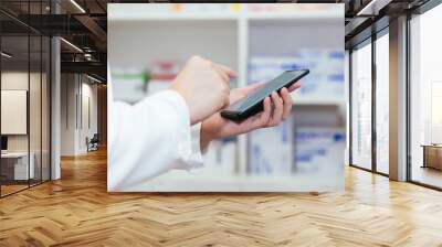 Pharmacist, Physician using a mobile phone at drugstore room. Doctor touching a cell phone in medical concept. Wall mural