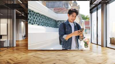 Portrait of Asian male traveler using a mobile phone on sidewalk of buddhist temple on street in Bangkok, Thailand, Southeast Asia - smart phone and internet for traveling concept Wall mural