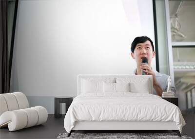 Portrait of young handsome Asian male speaker publicly speaking on stage to group of audience with white board behind Wall mural