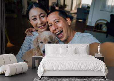 Young adult Asian couple holding a puppy taking a selfie from a phone with home interior in background. 30s mature man and woman with dog pet taking a family photo shots. - Happy group portrait Wall mural