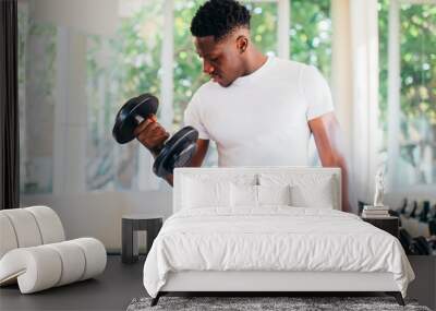 Young African American man standing and lifting a dumbbell with the rack at gym. Male weight training person doing a biceps curl in fitness center Wall mural