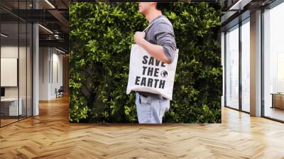 Young male hipster holding and carrying the Save The Earth tote handbag in green nature environment background - ecology and recycle concept. Wall mural