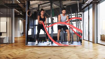 Athletic young couple with battle rope doing exercise in functional training fitness gym. Wall mural