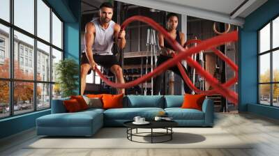 Athletic young couple with battle rope doing exercise in functional training fitness gym. Wall mural