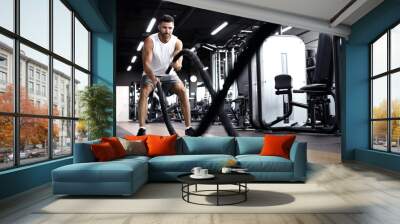 Athletic young man with battle rope doing exercise in functional training fitness gym. Wall mural