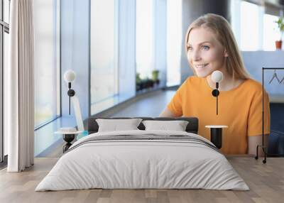 Beautiful business woman is using her smartphone with smile while sitting at her working place Wall mural