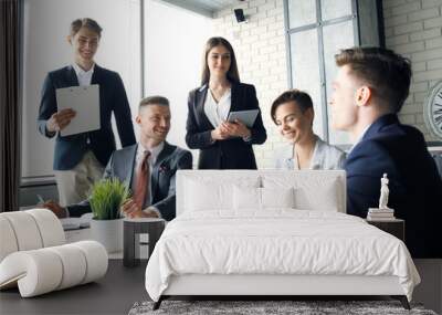 Brainstorm. Group of business people looking at the laptop together. One business woman looking at camera. Wall mural