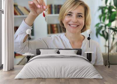 Cheerful middle aged female, real estate agent, sitting on couch, holding keys to new house. Wall mural