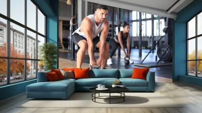 Fit and muscular couple focused on lifting a dumbbell during an exercise class in a gym. Wall mural