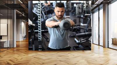 Fit and muscular indian man focused on lifting a dumbbell during an exercise class in a gym. Wall mural