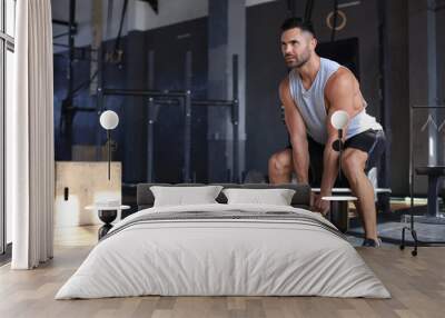 Fit and muscular man focused on lifting a dumbbell during an exercise class in a gym. Wall mural