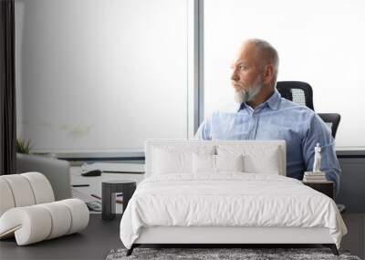 focused mature businessman deep in thought while sitting at a table in modern office. Wall mural