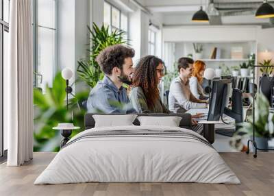 Group of young people in casual wear sitting at the office desk and discussing something while looking at PC together. Wall mural