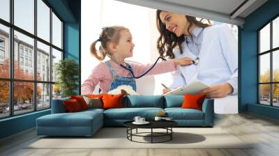 Little girl at the doctor for a checkup. Child auscultate the heartbeat of the doctor. Wall mural