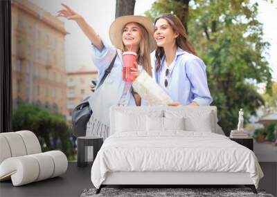 Photo of two girls enjoying sightseeing outdoor. Beautiful female tourists exploring city with map. Wall mural