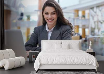 Portrait of a cheerful young businesswoman sitting at the table in office and looking at camera. Wall mural