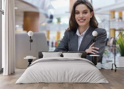 Portrait of a cheerful young businesswoman sitting at the table in office and looking at camera. Wall mural