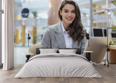 Portrait of a cheerful young businesswoman sitting at the table in office and looking at camera. Wall mural